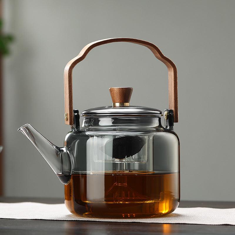 Tetera de cristal transparente con té negro y taza de té vacía