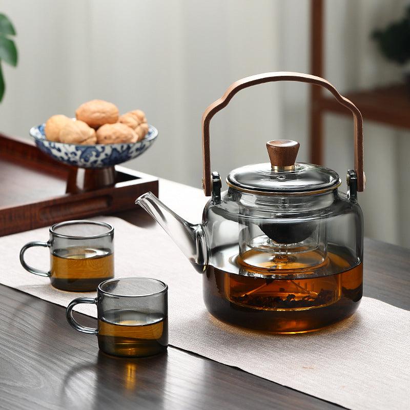Tetera de cristal transparente con té negro y taza de té vacía